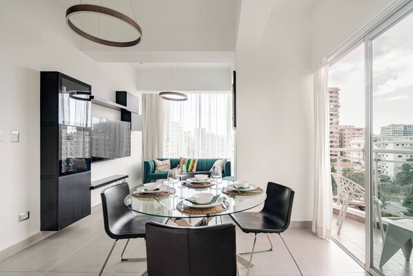 A modern dining area with a glass table, black chairs, and a teal sofa. - Step Into Elegance and Comfort (Santo Domingo)