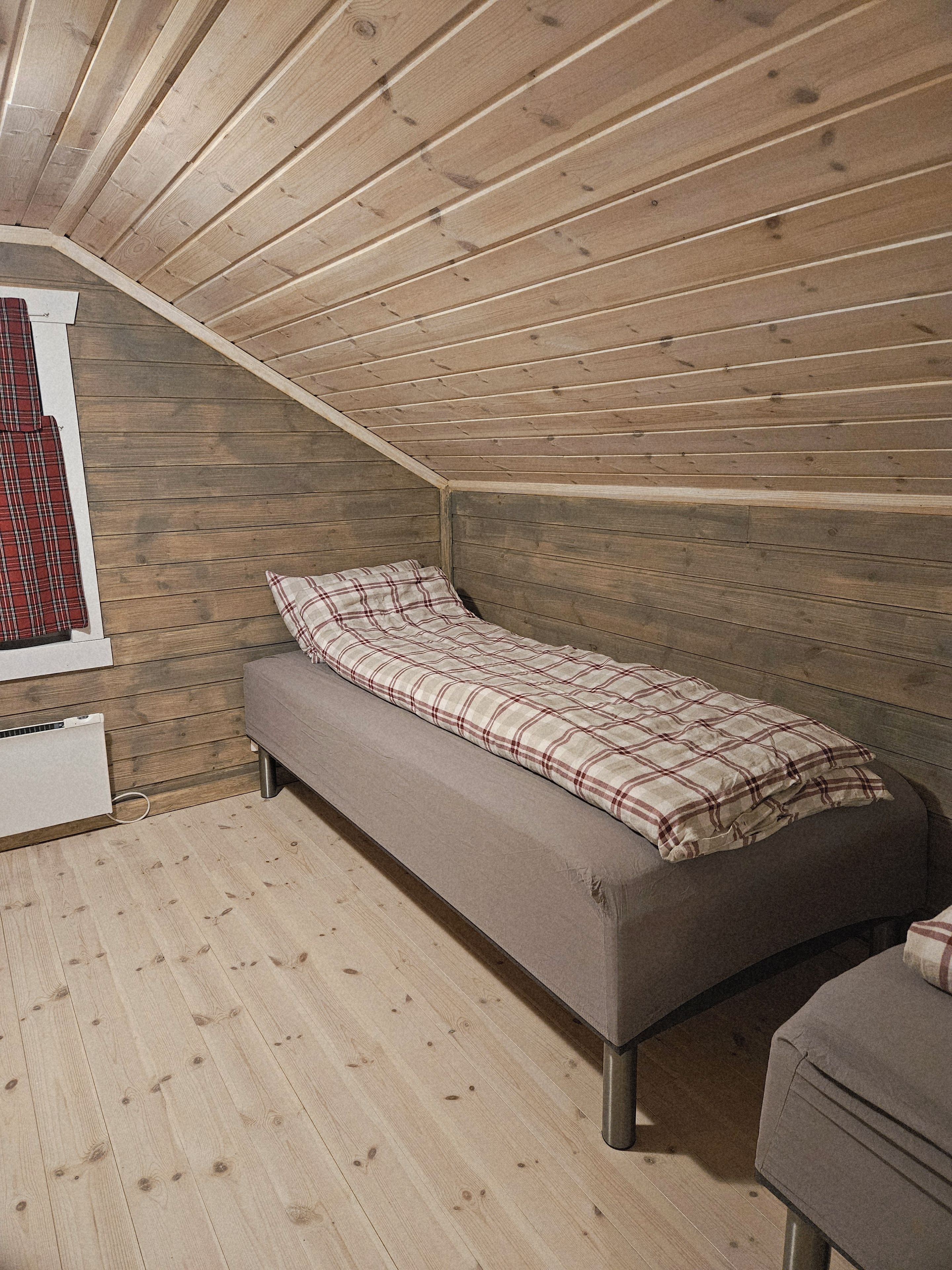 A single bed in a room with wooden walls and a sloped ceiling.