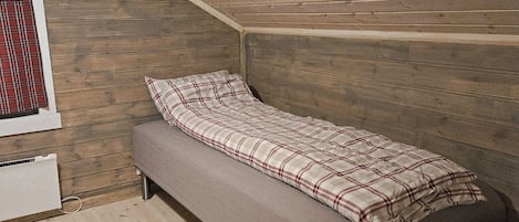Una cama individual en una habitación con paredes de madera y techo inclinado.