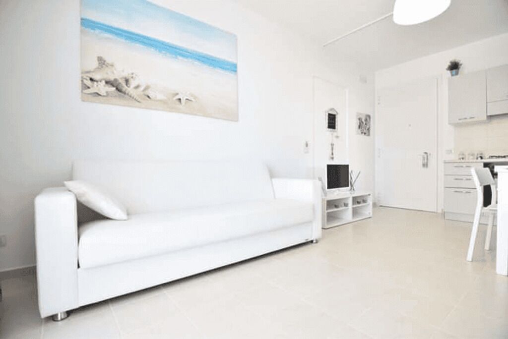 A modern living room with a white sofa, a flat-screen TV, and a painting of a beach scene.