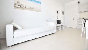 Uma sala de estar moderna com um sofá branco, uma TV de tela plana e uma pintura de uma cena de praia.
