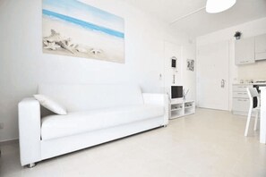 Ein modernes Wohnzimmer mit einem weißen Sofa, einem Flachbildfernseher und einem Gemälde einer Strandlandschaft.