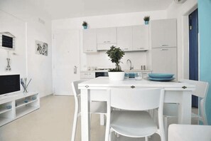 Eine moderne Küche mit weißen Schränken, einem Esstisch mit Stühlen und einem Blumentopf auf dem Tisch.