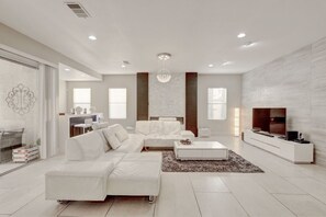 A modern living room with a white sofa, a coffee table, and a TV stand. - Extraordinary 6-bedroom house with in vibrant South west Las Vegas (Las Vegas)