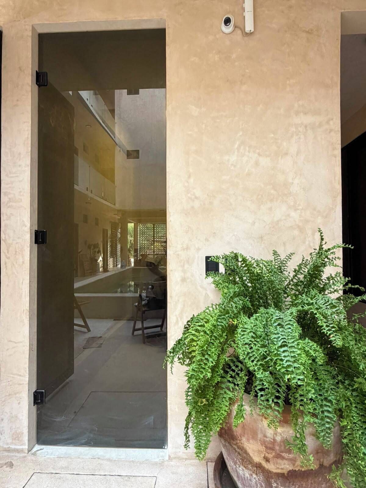 An entrance with a potted plant, a door, and a glimpse of an interior space with a table and chairs.