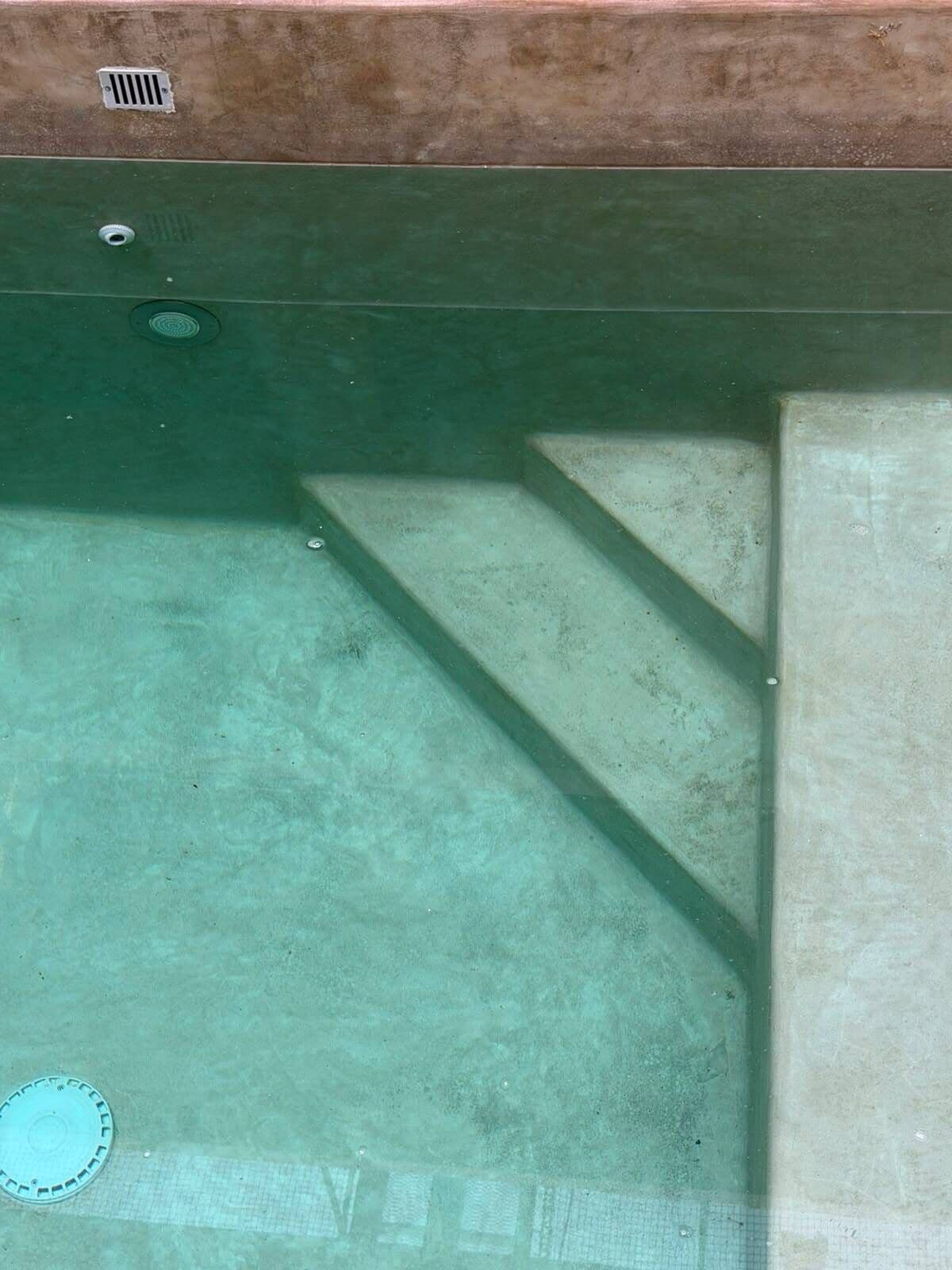 Una piscina con agua cristalina, escalones de acceso y una tapa de desagüe.
