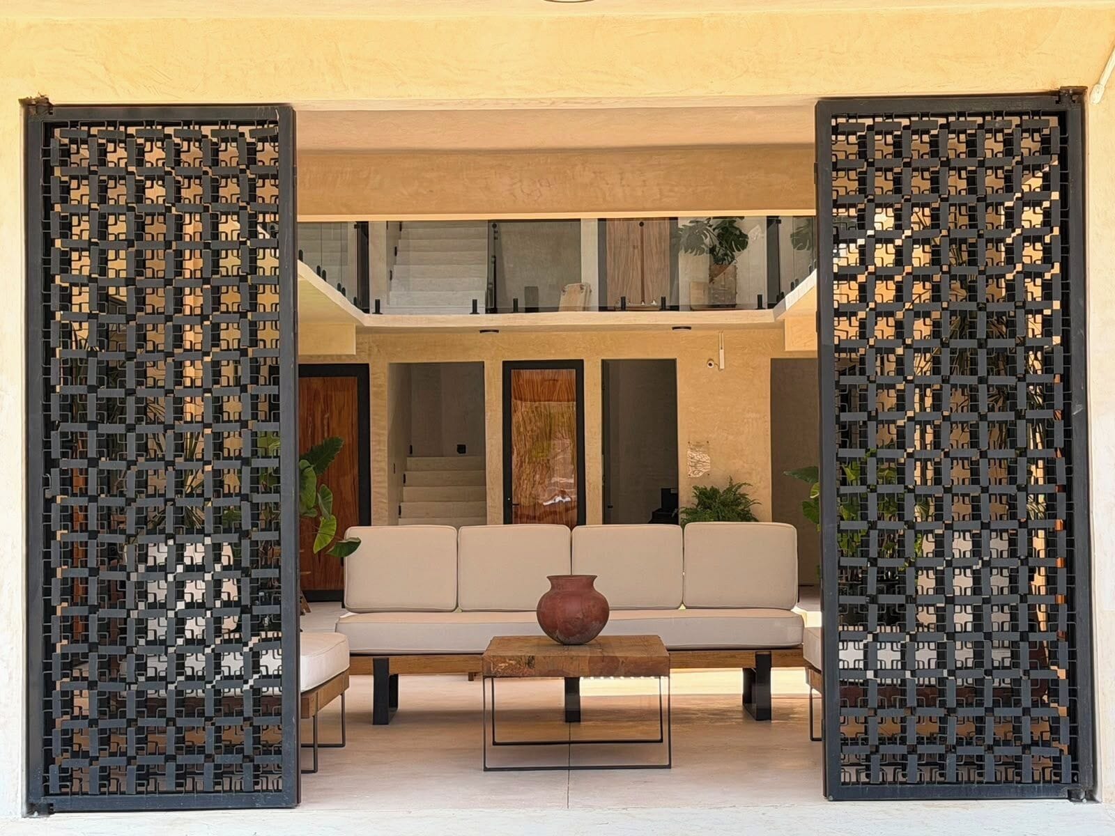 A modern living room with a sofa and coffee table, a staircase leading to a balcony, and decorative screens.