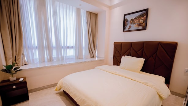 Habitación de hotel con una cama grande, una mesita de noche, una ventana con cortinas y un cuadro en la pared.