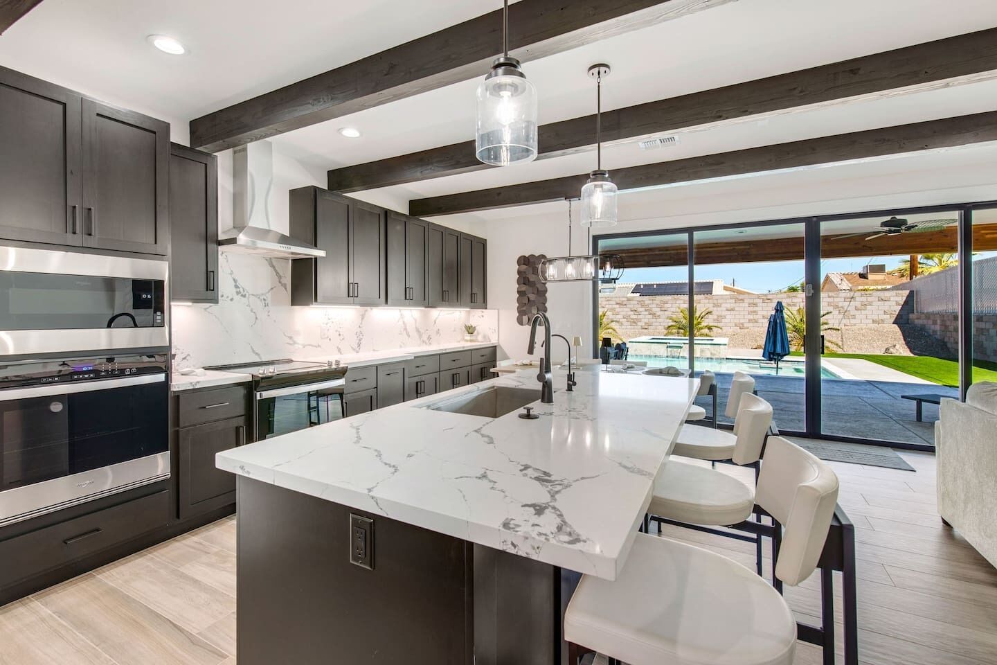 A modern kitchen with dark cabinetry, a marble countertop, and pendant lighting.