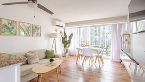 Ein modernes Wohnzimmer mit Sofa, Couchtisch und Essbereich, mit Holzboden und großen Fenstern.