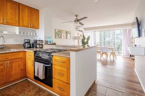 A modern kitchen with wooden cabinets, a stove, and a dining area with a table and chairs. - New Waikiki 2BR •Walk to Beach +free parking (Honolulu)