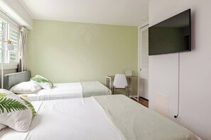 A hotel room with two beds, a desk, a chair, and a TV on the wall. - New Waikiki 2BR •Walk to Beach +free parking (Honolulu)