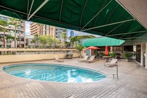 An outdoor swimming pool with lounge chairs and a barbecue area, surrounded by a covered patio. - New Waikiki 2BR •Walk to Beach +free parking (Honolulu)
