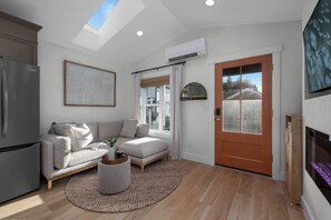 A modern living room with a sofa, a coffee table, and a wooden floor. - Seabrook Cottage - Couples + Small Families, BBQ, Indoor & Outdoor Fire (Pacific Beach)