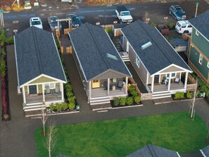 A row of single-story buildings with attached porches, a parking lot, and a green lawn. - Seabrook Cottage - Couples + Small Families, BBQ, Indoor & Outdoor Fire (Pacific Beach)