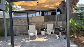 A covered patio area with a wooden fence, two white chairs, a grill, and a potted plant. - Aparment Downtown Sarasota 2br, 2ba, Petfriendly Beaches, 5 People (Sarasota)