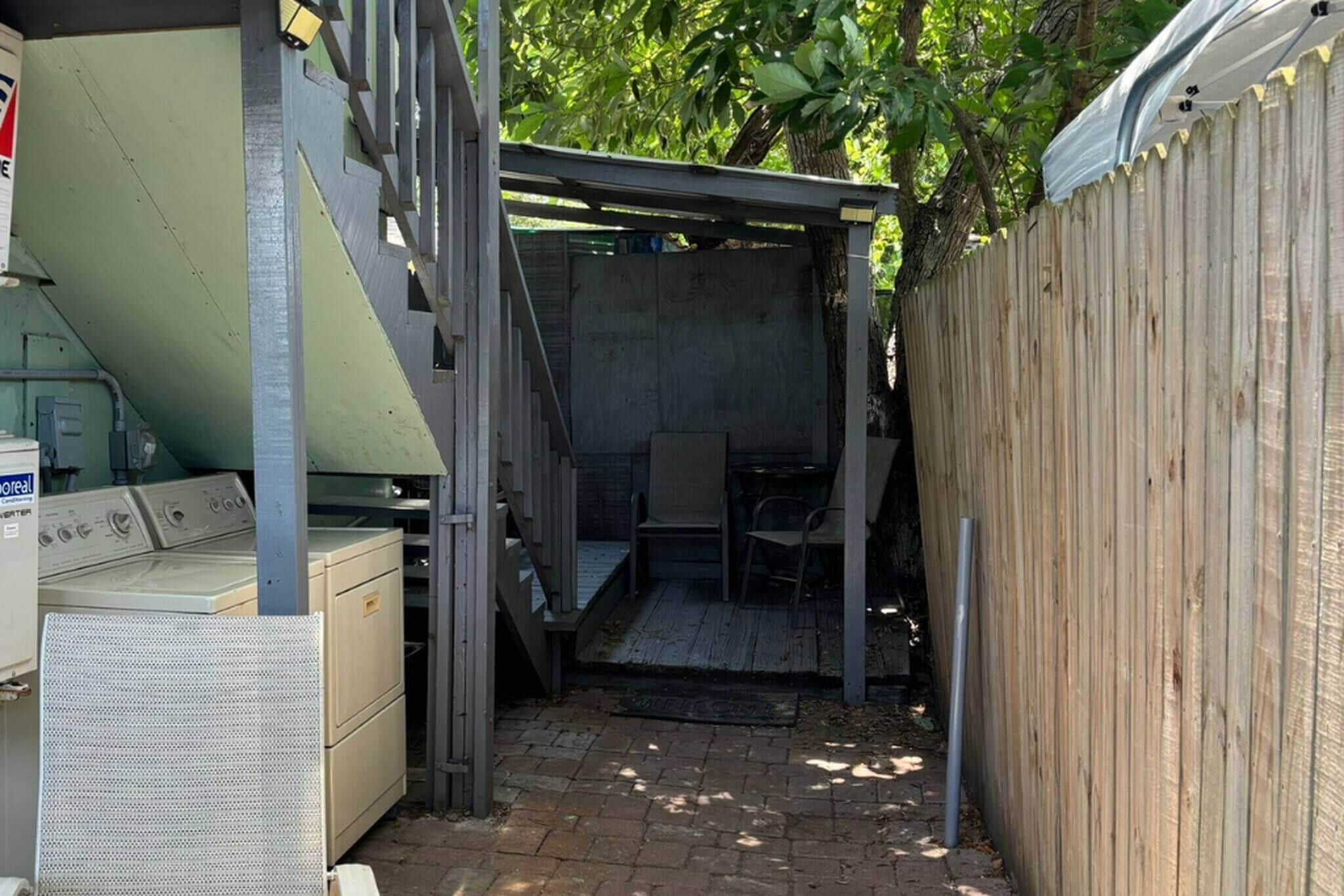 A small, enclosed outdoor space with a wooden fence, a metal staircase, and a bench.