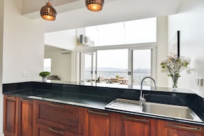 A modern kitchen with a black countertop, wooden cabinets, a stainless steel sink, and pendant lighting.