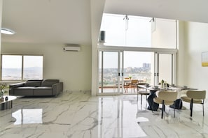 A spacious living area with a large window, a sofa, and a dining table with chairs.