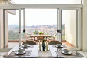 A dining area with a table set for four, overlooking a cityscape through large windows.