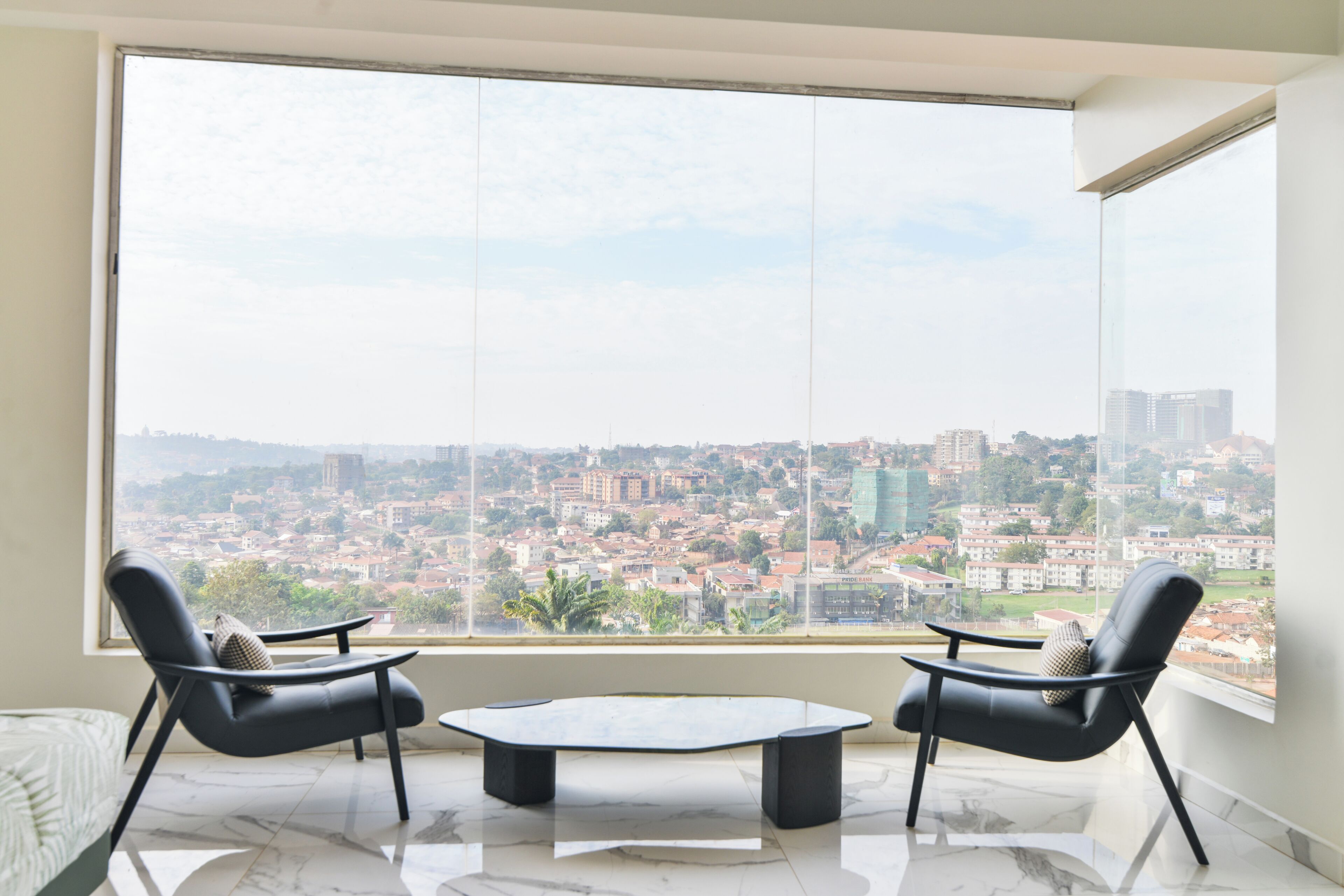 A room with a large window, two black chairs, a small table, and a view of a cityscape.