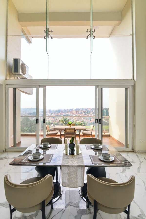 Comedor con una mesa lista para cuatro personas, ventanas amplias y vista a la ciudad.