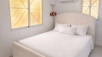 Ein Schlafzimmer mit einem großen Bett, zwei Fenstern mit Jalousien, einer Klimaanlage und einer roten Uhr an der Wand.