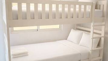 A bunk bed with a white frame and mattress, a window with blinds, and a tiled floor.
