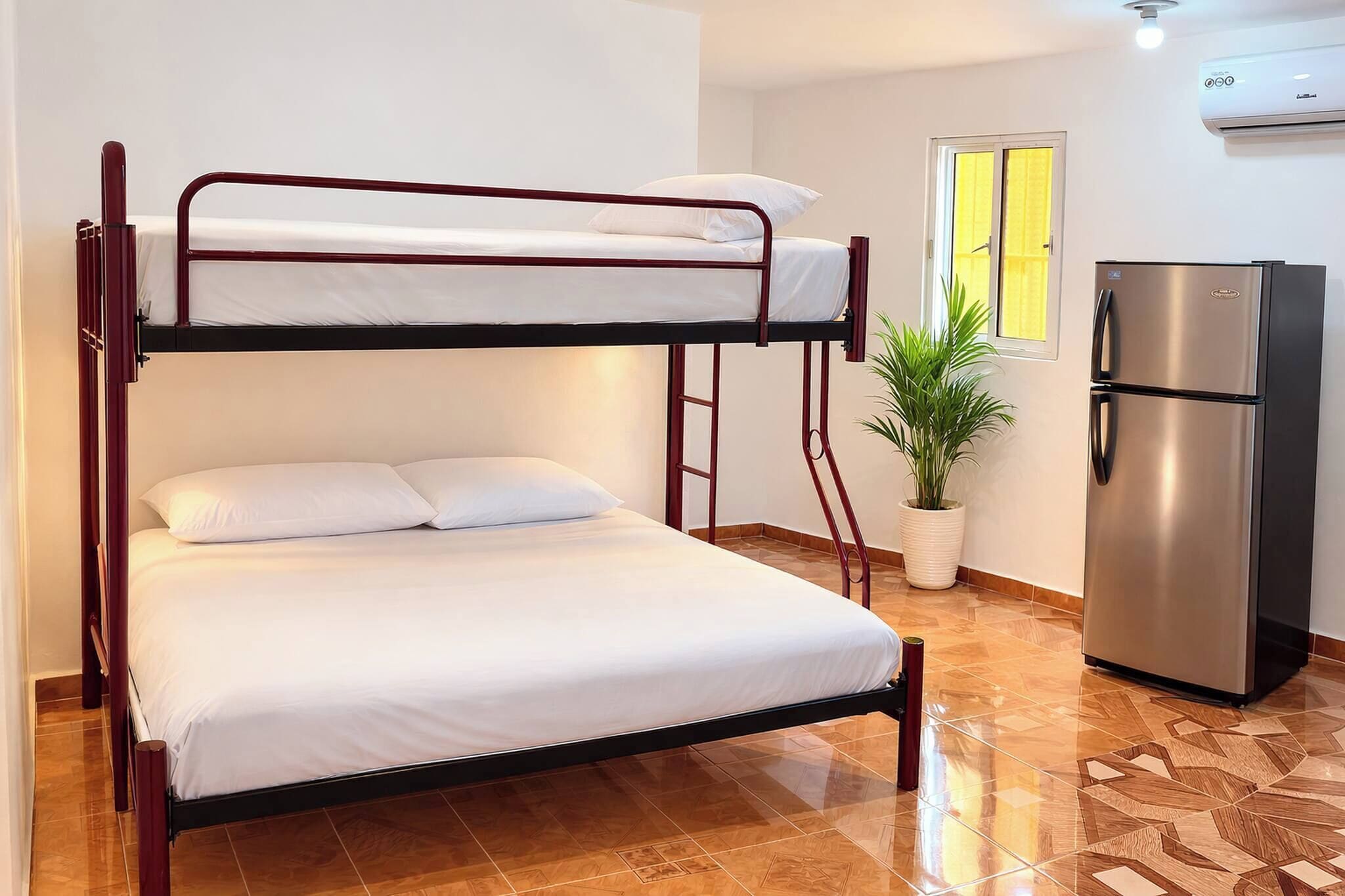 A bunk bed with a refrigerator and a potted plant in a room with tiled flooring.