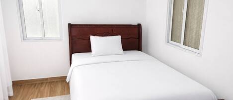 A bedroom with a wooden bed, white bedding, a white rug, and two windows with curtains.