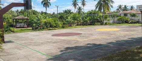 Una cancha de baloncesto al aire libre con un pabellón, palmeras y un edificio en el fondo.