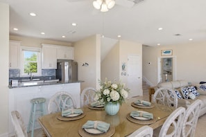 A modern kitchen with white cabinets, stainless steel appliances, and a dining area with a wooden table set for four. - The Blue Pelican New-SGI- POOL - Sleeps 12 (Eastpoint)