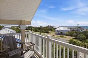 A balcony with a wooden chair and a table, overlooking a residential area with houses and a clear sky. - The Blue Pelican New-SGI- POOL - Sleeps 12 (Eastpoint)