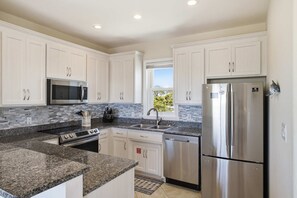 A modern kitchen with white cabinets, stainless steel appliances, and a granite countertop. - The Blue Pelican New-SGI- POOL - Sleeps 12 (Eastpoint)