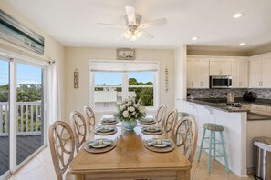 A dining area with a table set for six, a ceiling fan, and a view through the window. - The Blue Pelican New-SGI- POOL - Sleeps 12 (Eastpoint)