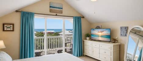 A bedroom with a large bed, a TV, a ceiling fan, and a view of the ocean.