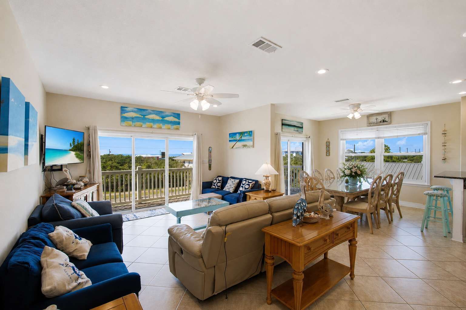 A spacious living area with a sofa, a coffee table, and a dining table with chairs. There is a balcony with a view of the beach.