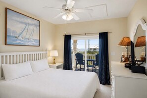 A hotel room with a bed, a ceiling fan, a painting of sailboats, a balcony with chairs, and a view of the ocean. - The Blue Pelican New-SGI- POOL - Sleeps 12 (Eastpoint)