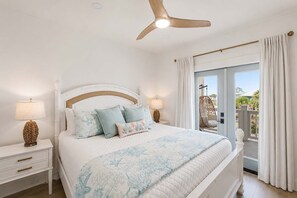 Un dormitorio con cama, mesitas de noche, ventilador de techo y vistas al exterior.