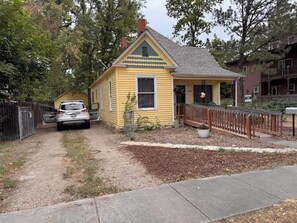 A yellow house with a fenced yard, a parked car, and a sidewalk. - Charming 3BR Home • 1 Block to Downtown • Fenced Yard (Longmont)