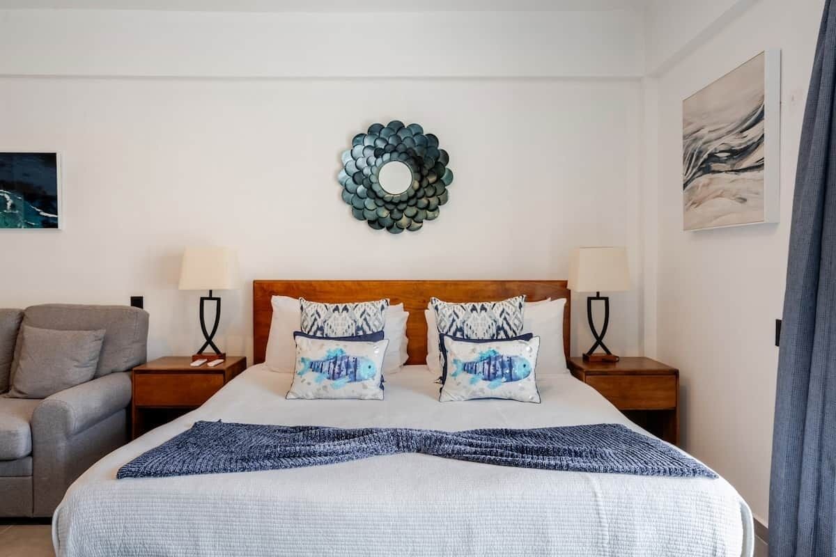 A hotel room with a bed, two nightstands, a lamp, a sofa, and decorative wall art.