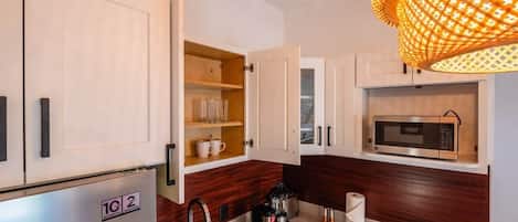 A compact kitchen with a refrigerator, microwave, coffee maker, and a hanging light fixture.