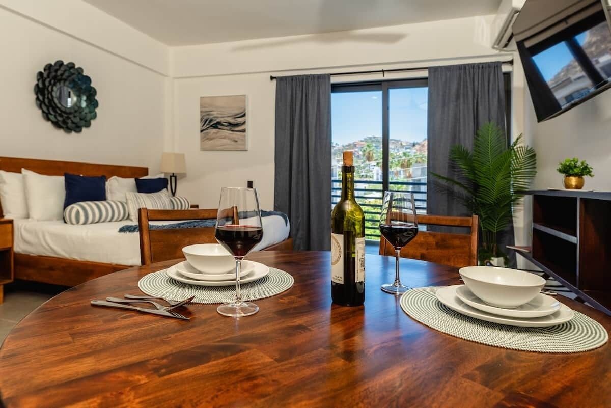 Une chambre d’hôtel avec une table à manger dressée pour deux personnes, un lit avec vue et un téléviseur fixé au mur.