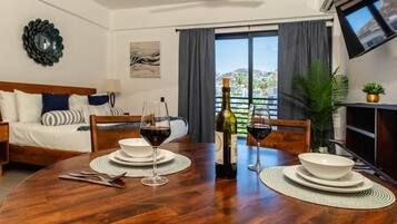 Une chambre d’hôtel avec une table à manger dressée pour deux personnes, un lit avec vue et un téléviseur fixé au mur.