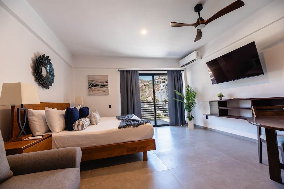 Une chambre d’hôtel équipée d’un lit, d’un bureau, d’une chaise, d’une télévision, d’un ventilateur de plafond et offrant une vue sur l’extérieur.
