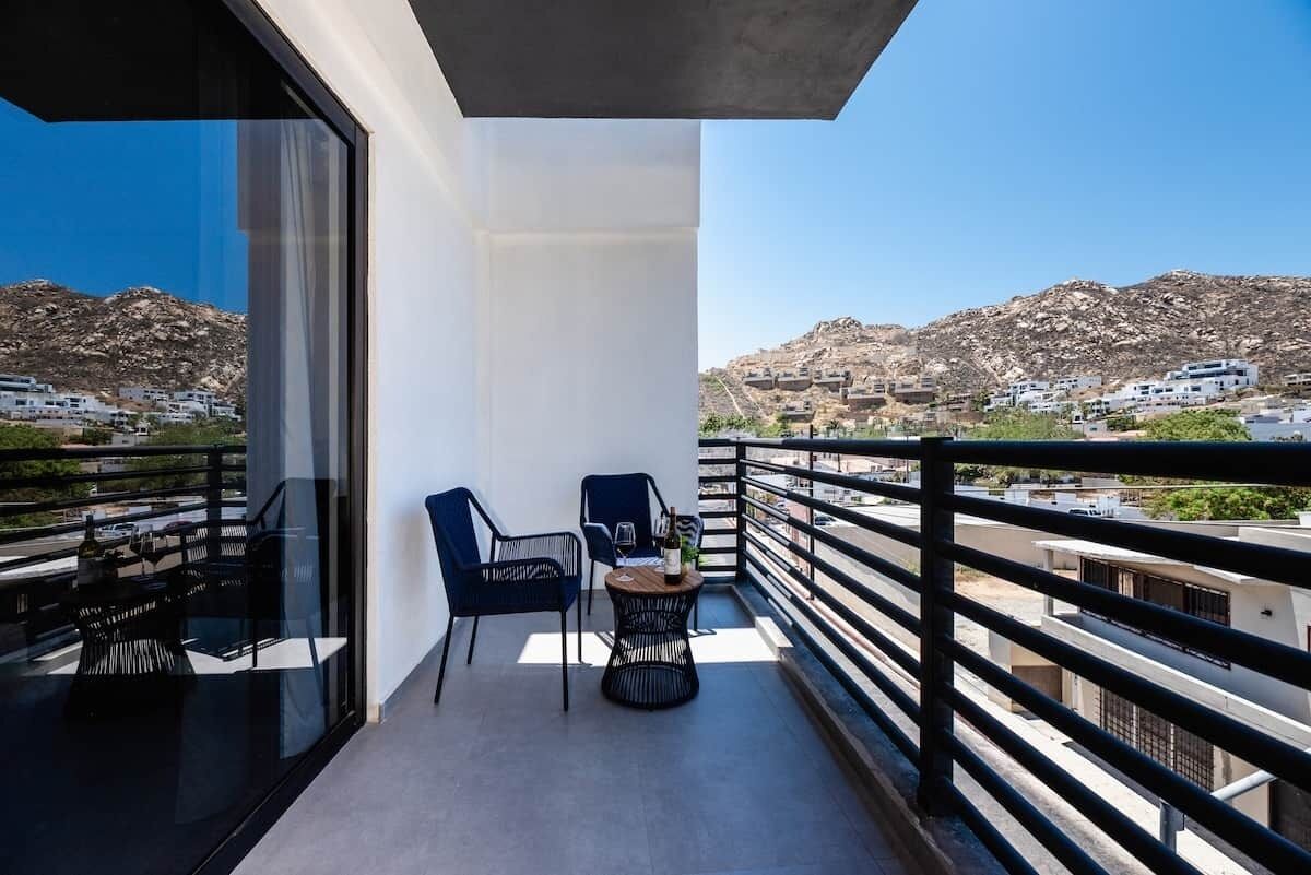 Un balcón con una mesa y sillas, con vistas a un paisaje montañoso y edificios.