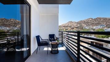 Un balcón con una mesa y sillas, con vistas a un paisaje montañoso y edificios.