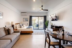 Une chambre d’hôtel moderne équipée d’un lit, d’un canapé, d’une table à manger pour deux personnes, d’un téléviseur fixé au mur et d’un balcon avec vue.