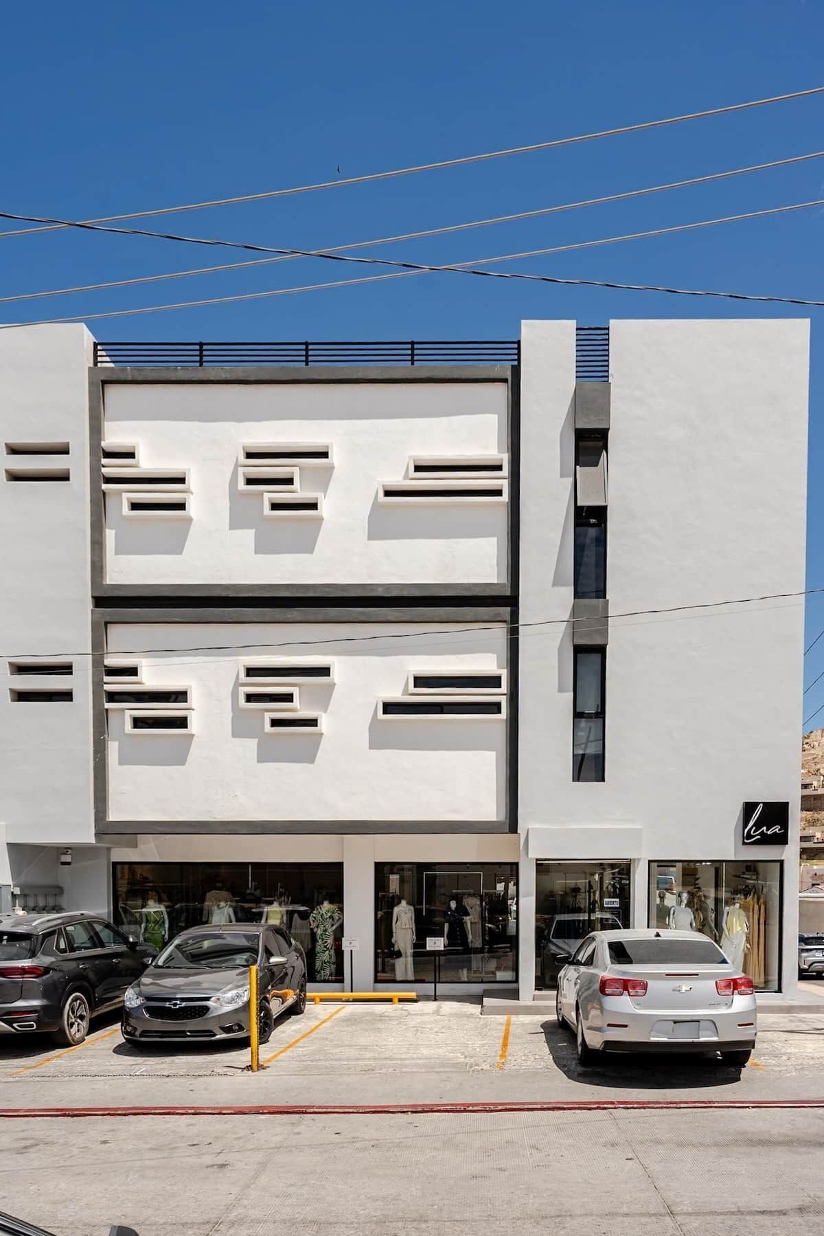 Un bâtiment moderne à la façade plate, doté de nombreuses fenêtres et comprenant un parking avec des voitures.