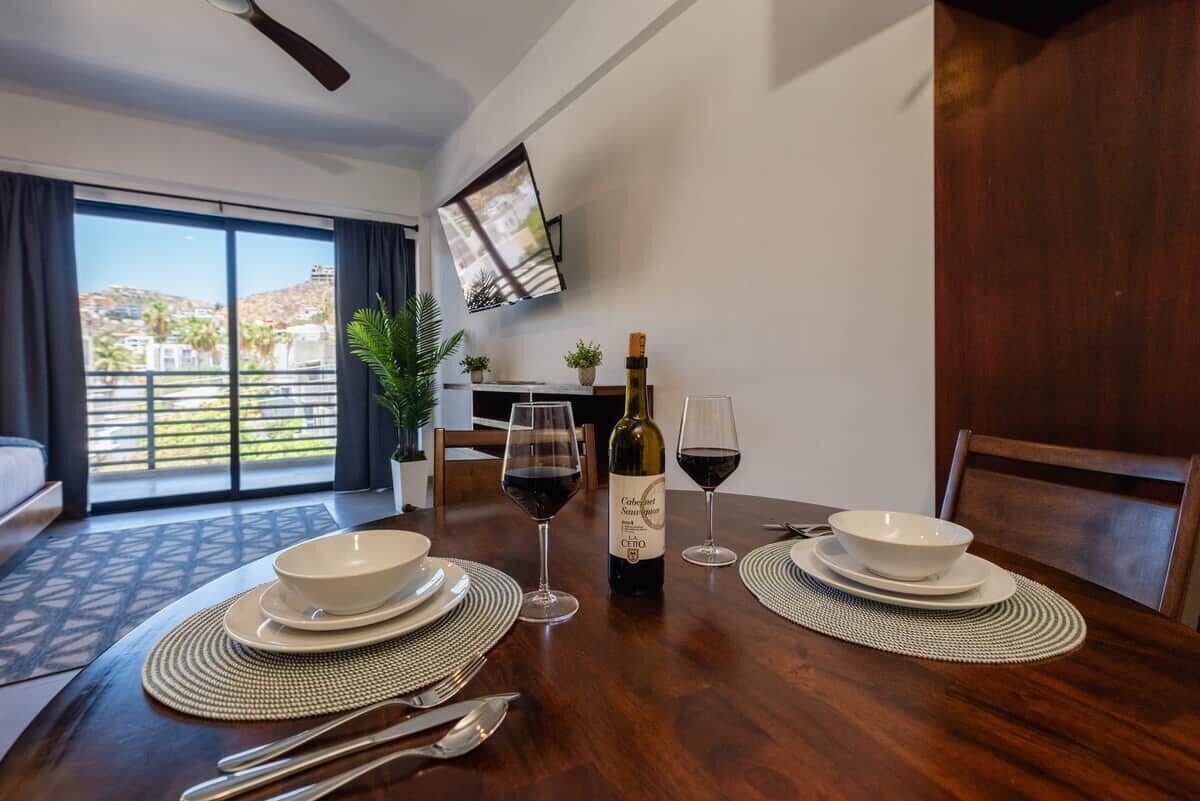 Een eethoek met een tafel gedekt voor twee personen, een fles wijn en een aan de muur bevestigde televisie.